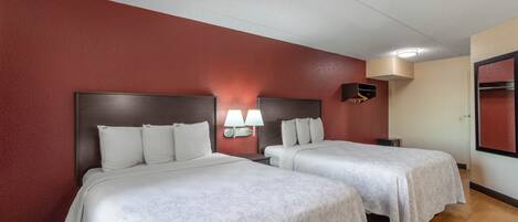 Habitación de hotel con dos camas, cada una con sábanas y almohadas blancas, una pared de acento roja y una lámpara fijada al techo.