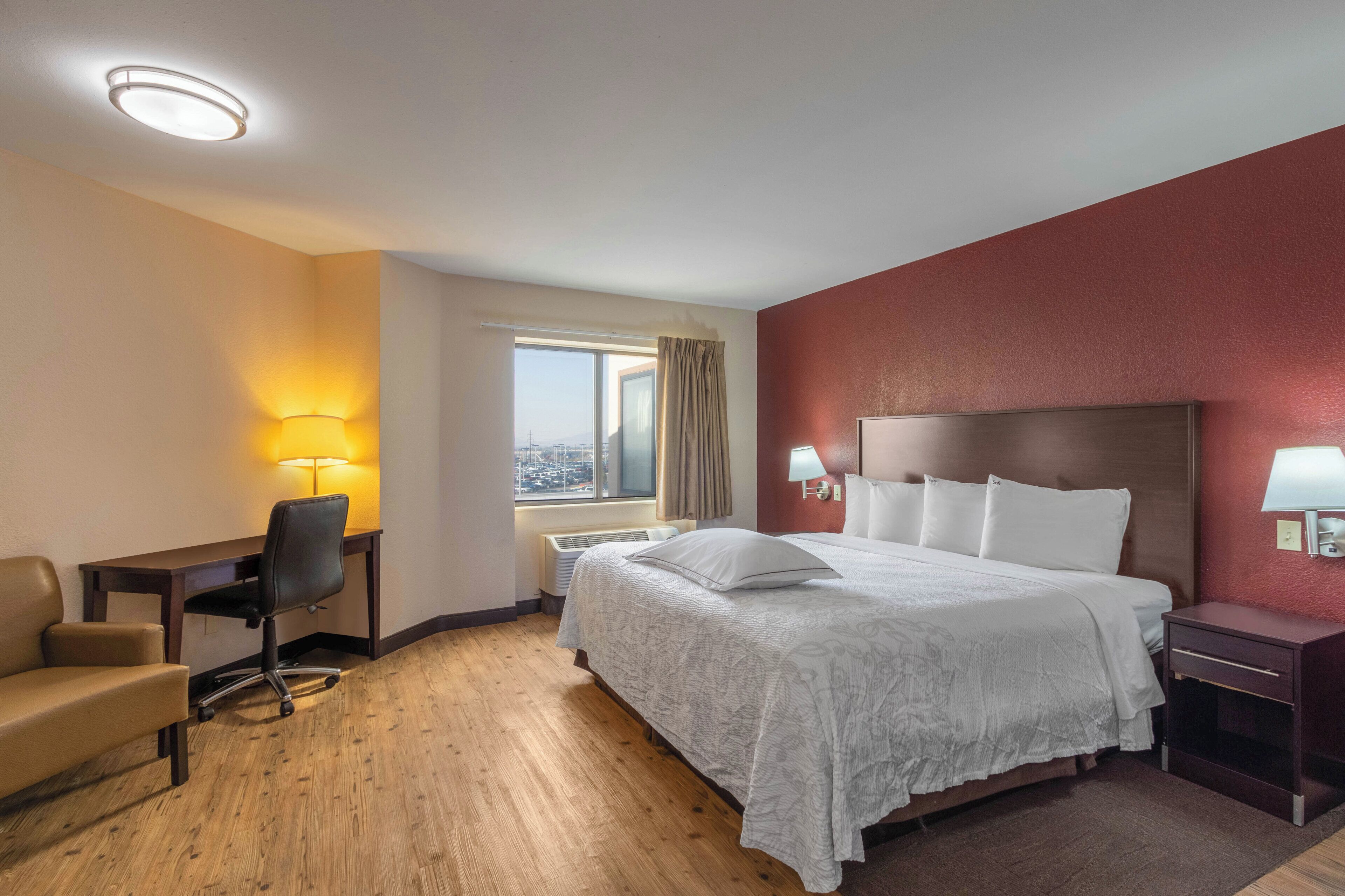 A hotel room with a bed, desk, chair, and a window with a view.
