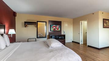 Una camera d'albergo con un letto, una televisione, una cassettiera, uno specchio e una porta.