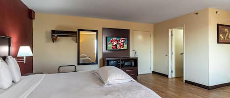 Una habitación de hotel con una cama, televisión, cómoda, espejo y puerta.