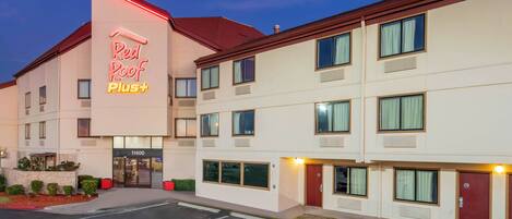 A hotel with a prominent Red Roof Plus sign, multiple floors, and a parking lot.