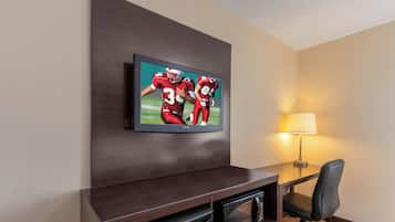 A hotel room with a flat-screen TV mounted on a dark wooden console, a Darty microwave, a black office chair, and a table lamp.