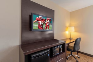 A hotel room with a flat-screen TV mounted on a dark wooden console, a Darty microwave, a black office chair, and a table lamp. - Red Roof Inn PLUS+ El Paso East (El Paso)