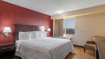 A hotel room with a large bed, two bedside lamps, a window with curtains, a chair, and a ceiling light.
