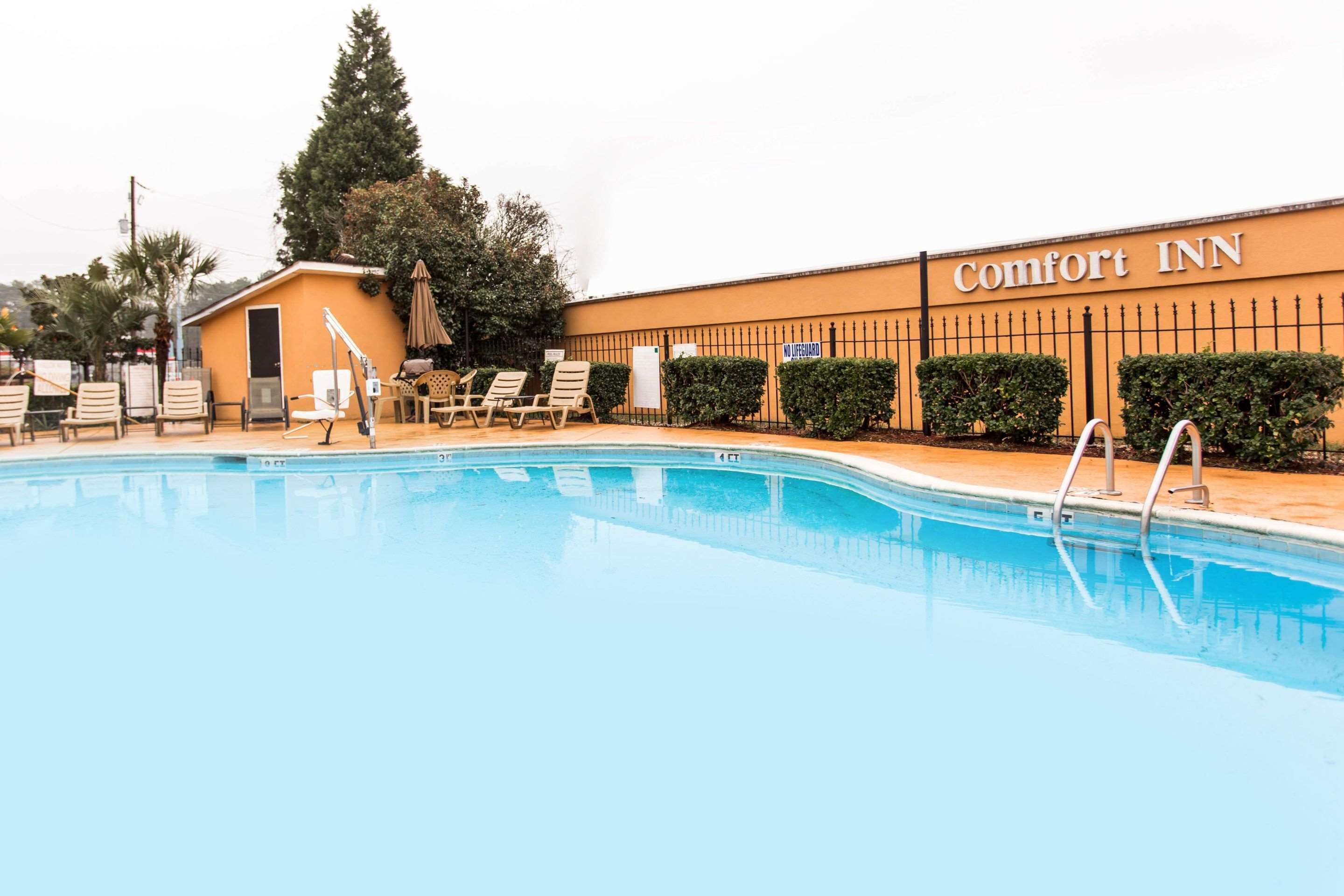 A Comfort Inn with a swimming pool, lounge chairs, and a small building with a door and window.