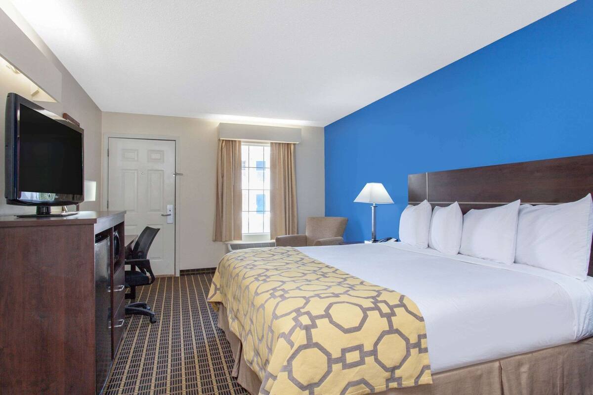 A hotel room with a bed, a desk, a television, a lamp, and a chair.