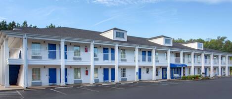 Un motel con una fila de habitaciones, cada una con un balcón y una puerta azul.