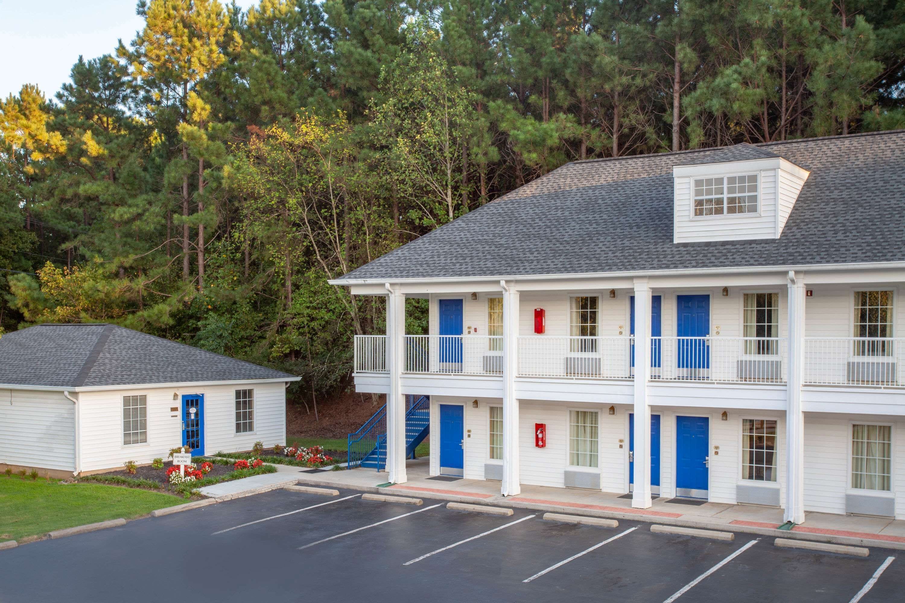 Un motel à deux étages avec une porte bleue, un petit bâtiment attenant et un parking.