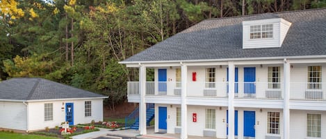 Ein zweistöckiges Motel mit blauer Tür, einem kleinen Anbau und einem Parkplatz.