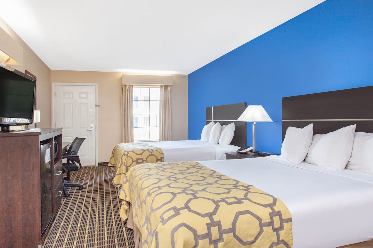 A hotel room with two beds, a desk with a TV, a chair, and a window with curtains.