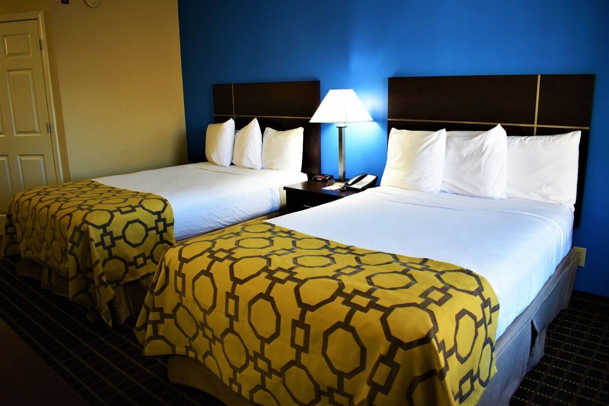 A hotel room with two beds, a nightstand with a lamp, and a telephone.