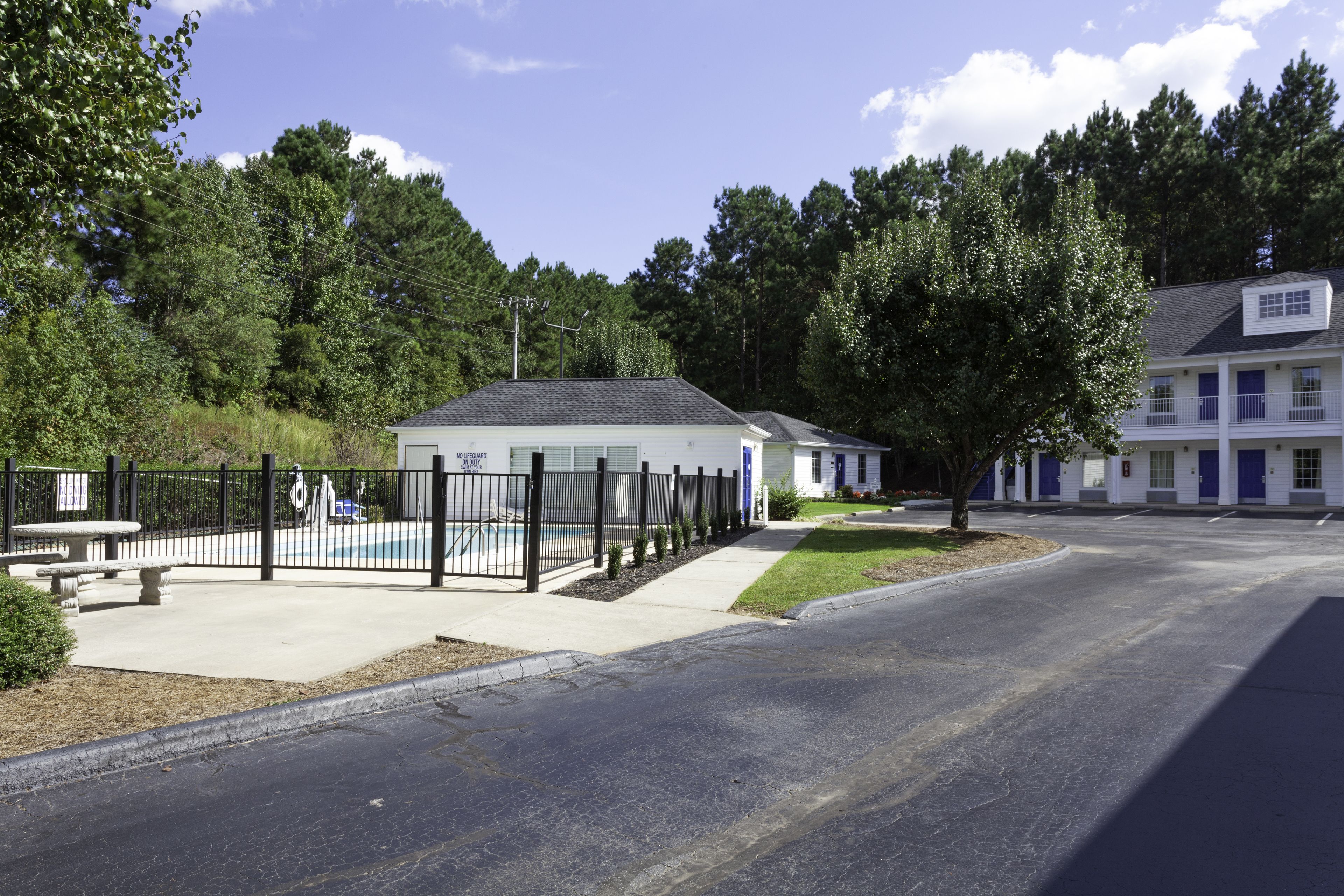 A residential building with a fenced pool area, a small patio, and a well-maintained lawn.