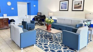 Un hall moderno de hotel con sofás azules, una alfombra estampada y un escritorio con computadora.