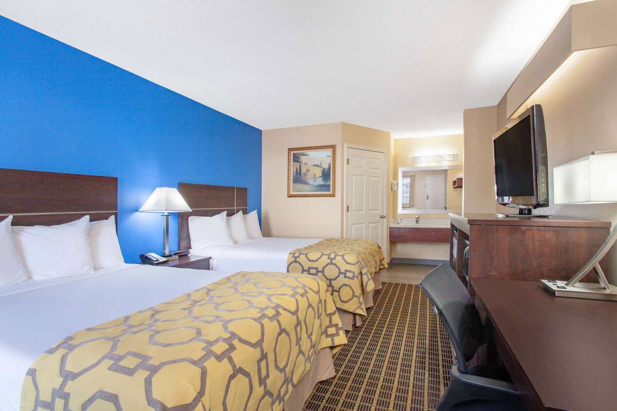 A hotel room with two beds, a desk, a television, and a bathroom visible in the background.