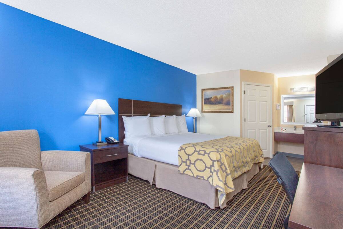A hotel room with a bed, bedside tables, a chair, a desk, and a television.
