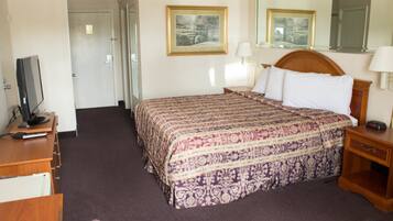 A hotel room with a bed, a desk with a television, a bedside table, and two framed pictures on the wall.