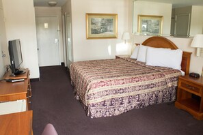 A hotel room with a bed, a desk with a television, a bedside table, and two framed pictures on the wall.
