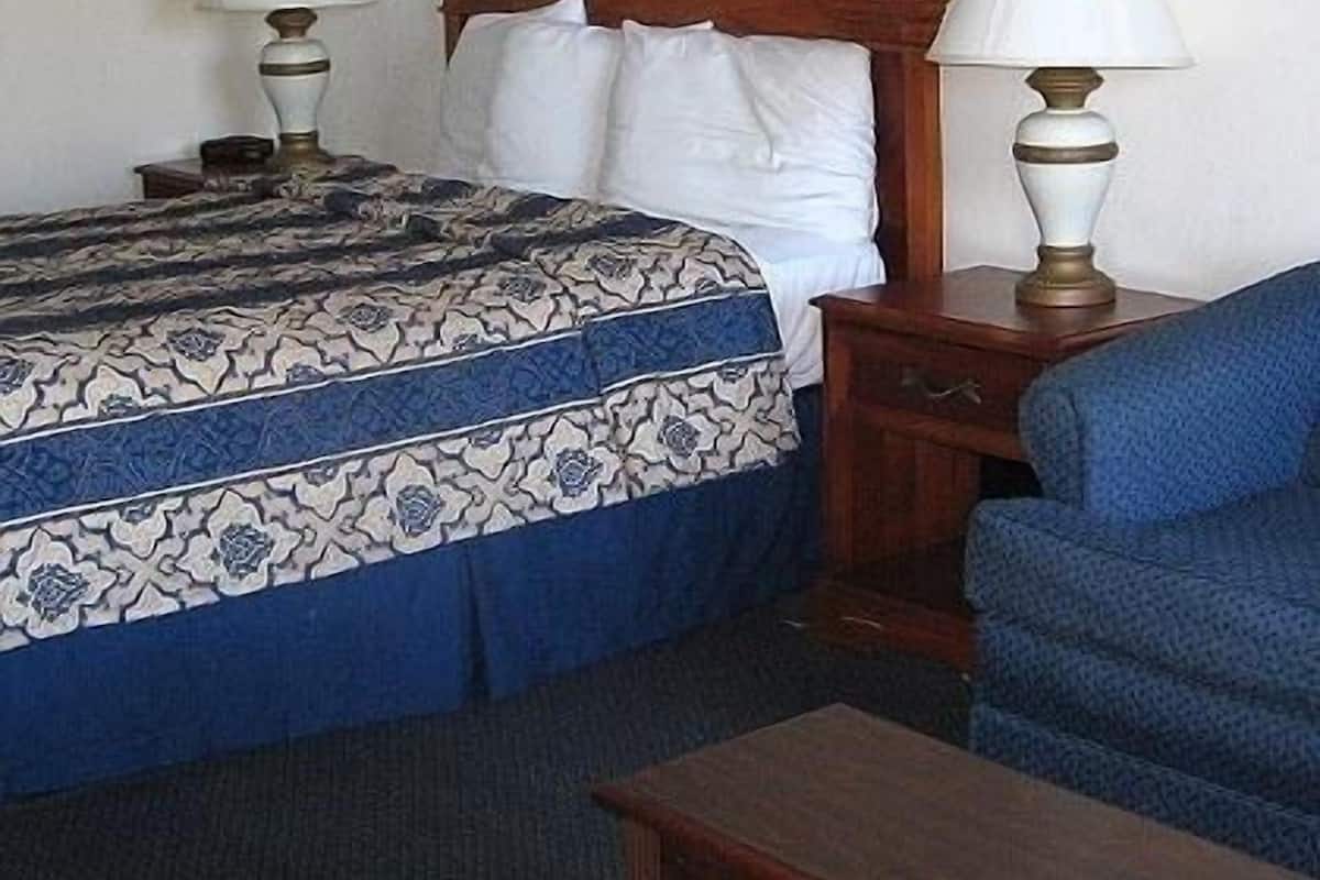 A hotel room with a bed, two bedside tables with lamps, a chair, and a small table.