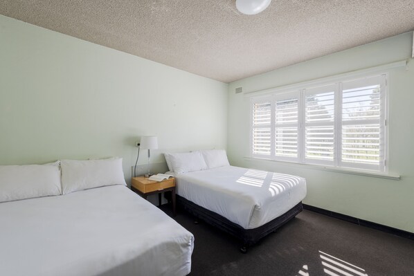 Une chambre d’hôtel avec deux lits simples, une table de chevet avec une lampe et une fenêtre avec des stores.