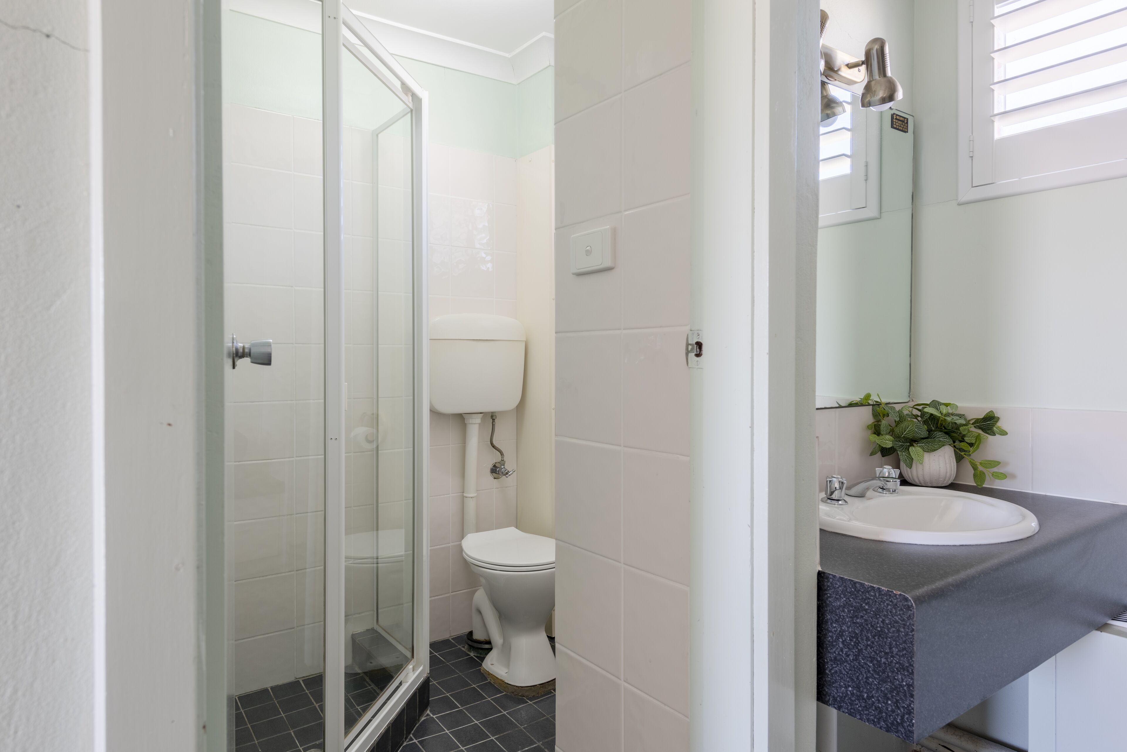 Un baño con cabina de ducha de vidrio, inodoro blanco y lavamanos con encimera oscura.