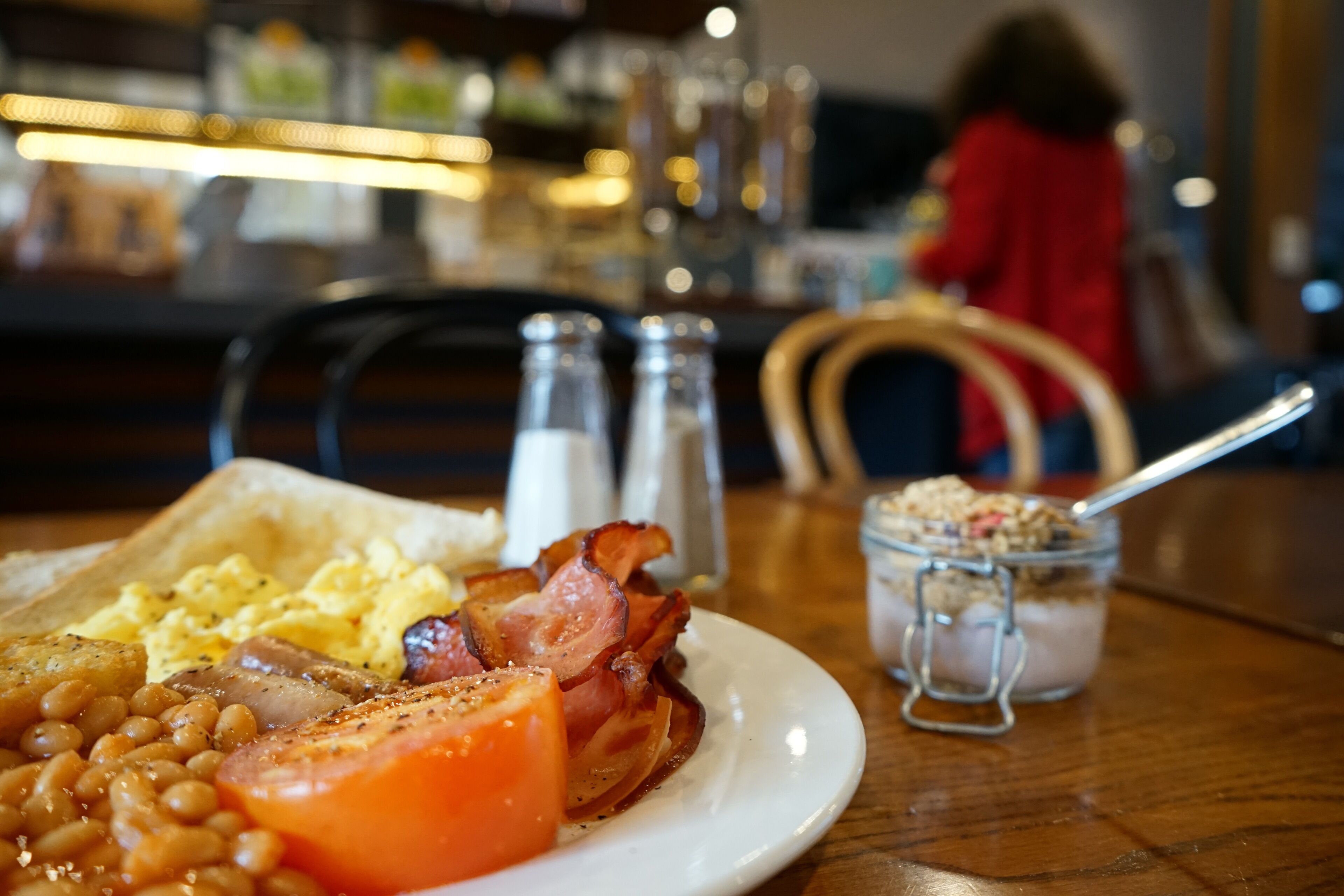 Un plato de desayuno con huevos, tocino, frijoles y tomate sobre una mesa de madera.