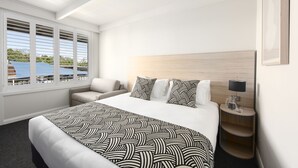 Ein Hotelzimmer mit einem großen Bett, einem Nachttisch mit Lampe, einem Sessel und einem Fenster mit Jalousien.