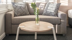 Ein modernes Wohnzimmer mit einem grauen Sofa, Kissen mit Schwarz-Weiß-Muster, einem runden Holztisch und einer Vase mit Blumen.
