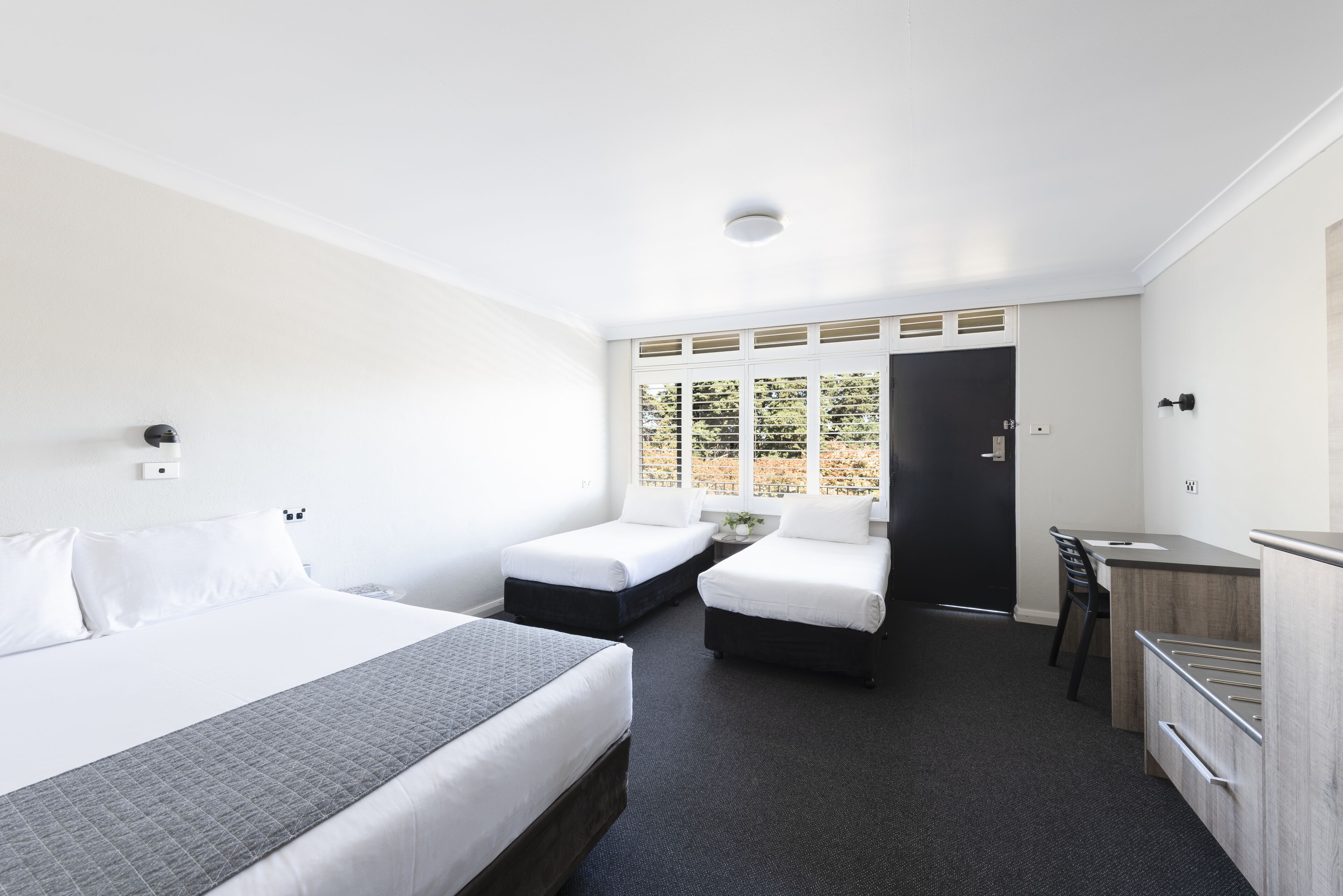 A modern hotel room with a large bed, two smaller beds, a desk, and a chair.