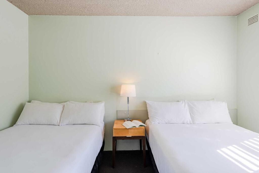 A twin room with two beds, a nightstand with a lamp, and a book.