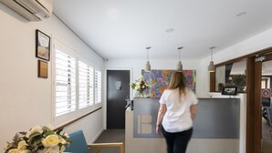 Ein Empfangsbereich mit einer Rezeption, einem blauen Sessel, einer Blumenvase und einem Wandbild.