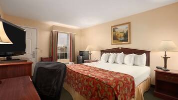 A hotel room with a large bed, a desk, a chair, a television, a desk lamp, and a painting on the wall.