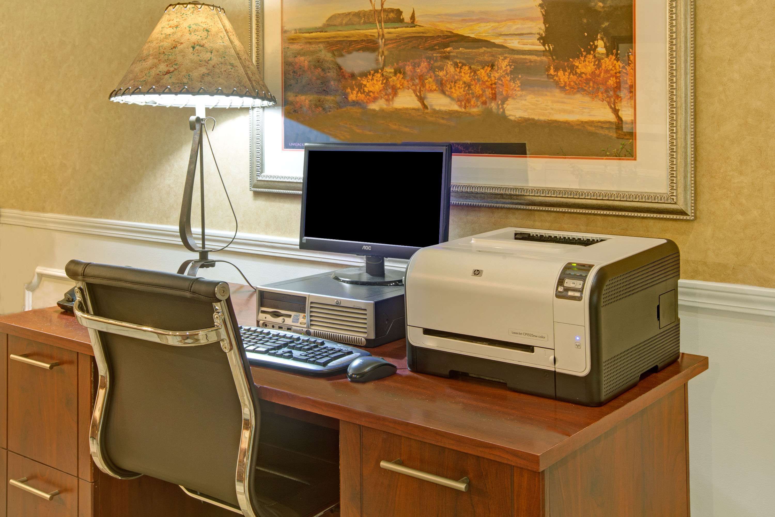A wooden desk with a computer, a lamp, a printer, and a chair.