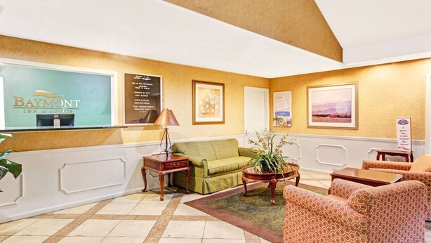 A hotel lobby with a reception desk, green sofa, patterned armchairs, and a potted plant.