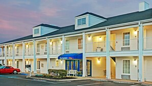 A motel with multiple rooms, a blue awning, and a red car parked in front.