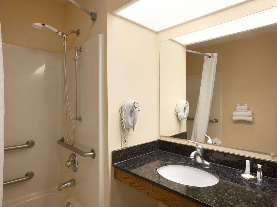 A bathroom with a shower, grab bars, a sink, and a mirror.