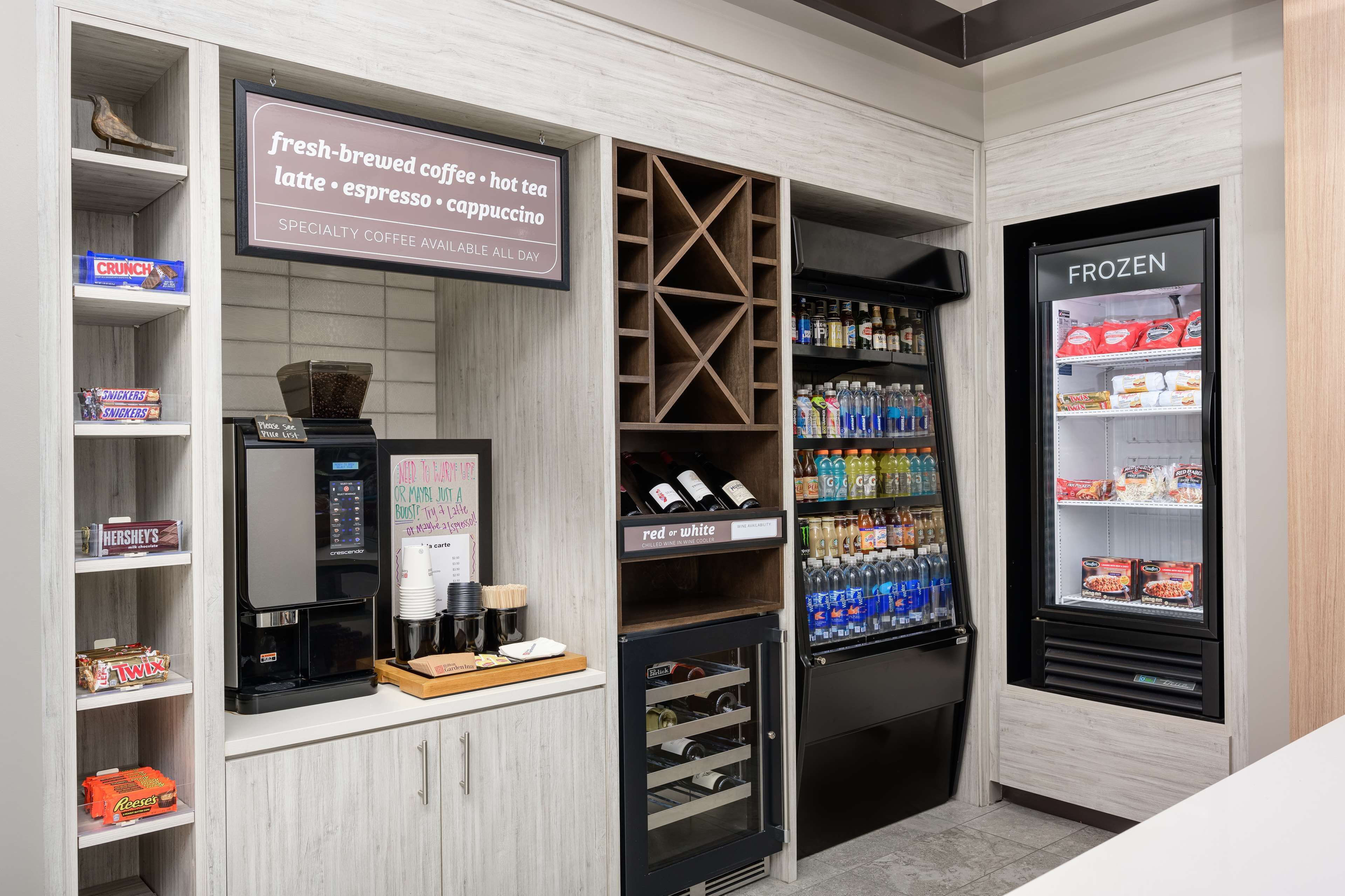 Uma cafeteria com máquina de café, prateleiras com lanches, um letreiro anunciando café fresco e um dispensador de bebidas geladas.
