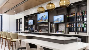 A modern bar area with a long counter, multiple seating options, and a variety of liquor bottles. - Hilton Garden Inn Knoxville Papermill Drive (Knoxville)