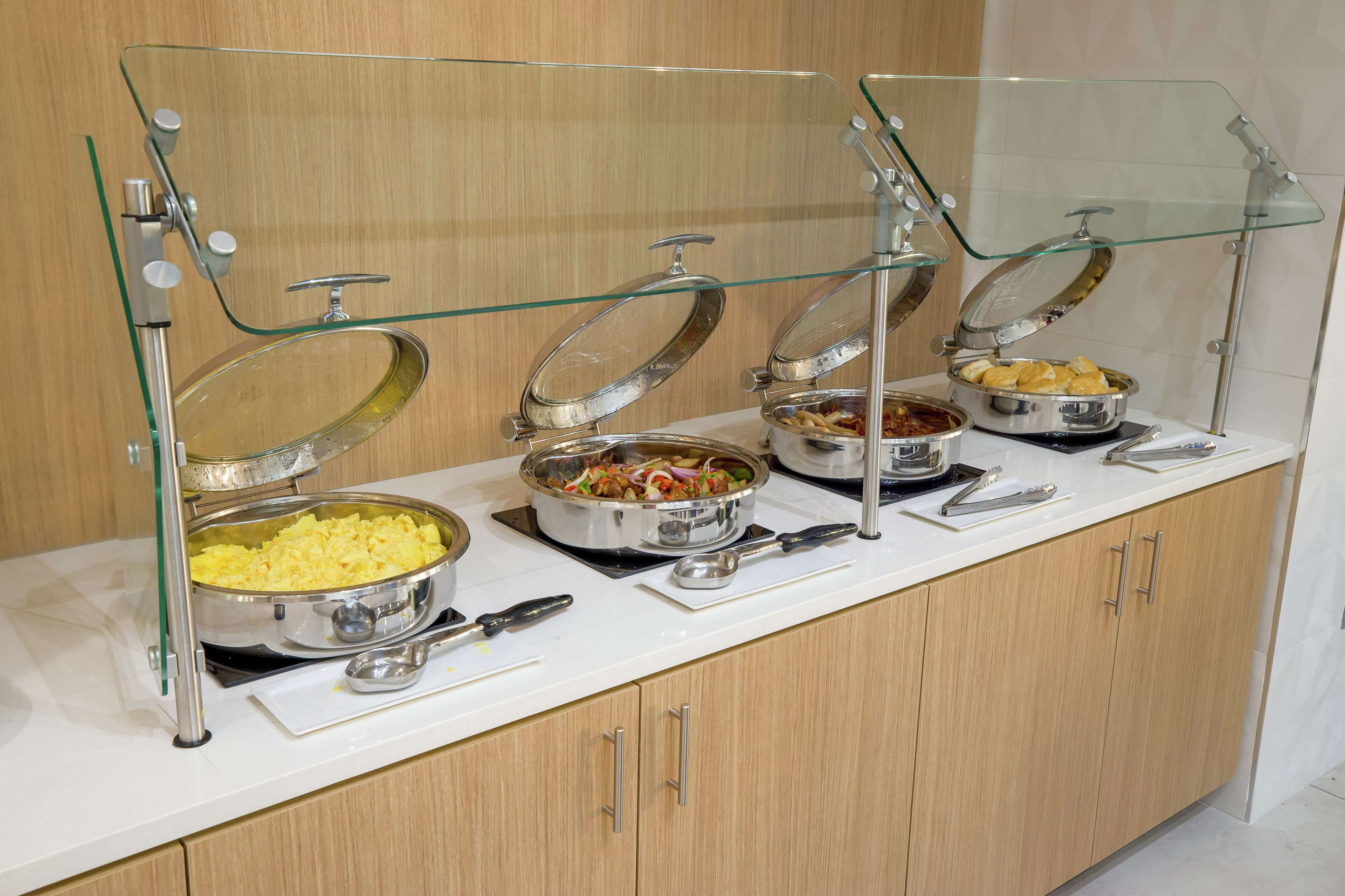 A buffet setup with multiple food stations, each with a glass cover and metal serving utensils.