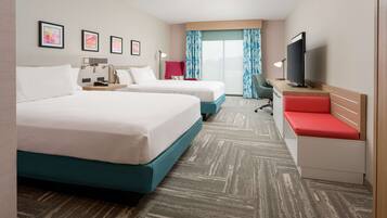 A hotel room with two beds, a desk with a TV, a chair, and a window with curtains.
