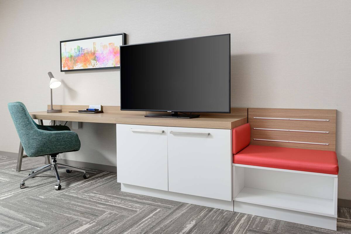 Un espacio de oficina moderno con escritorio, silla y un televisor de pantalla plana grande.