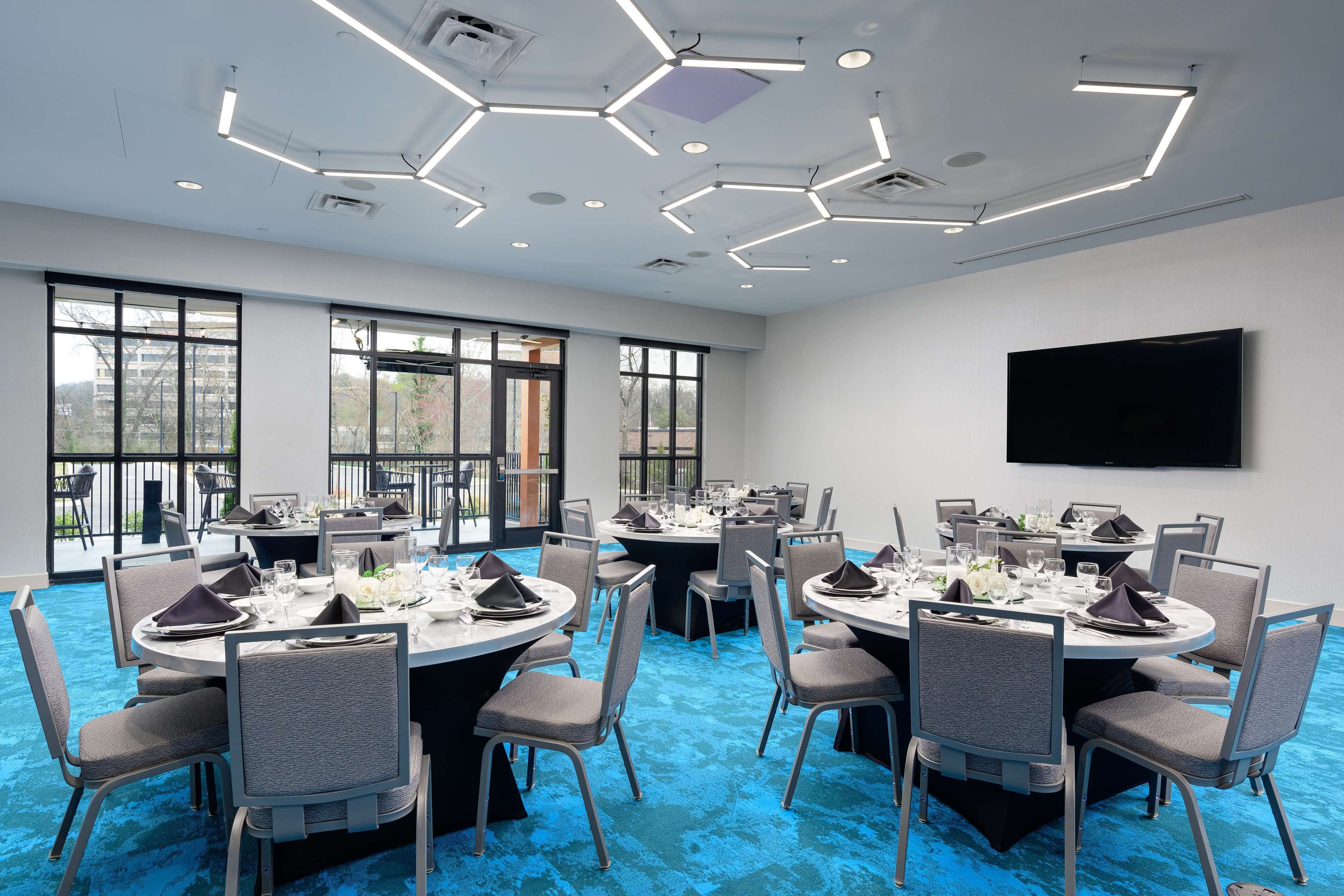 A conference room with round tables, chairs, and a flat-screen TV on the wall.