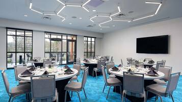 A conference room with round tables, chairs, and a flat-screen TV on the wall.