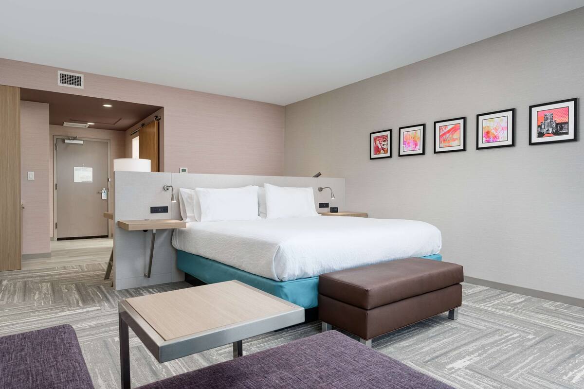 Una habitación de hotel moderna con cama, mesita de noche y una pequeña zona de estar.