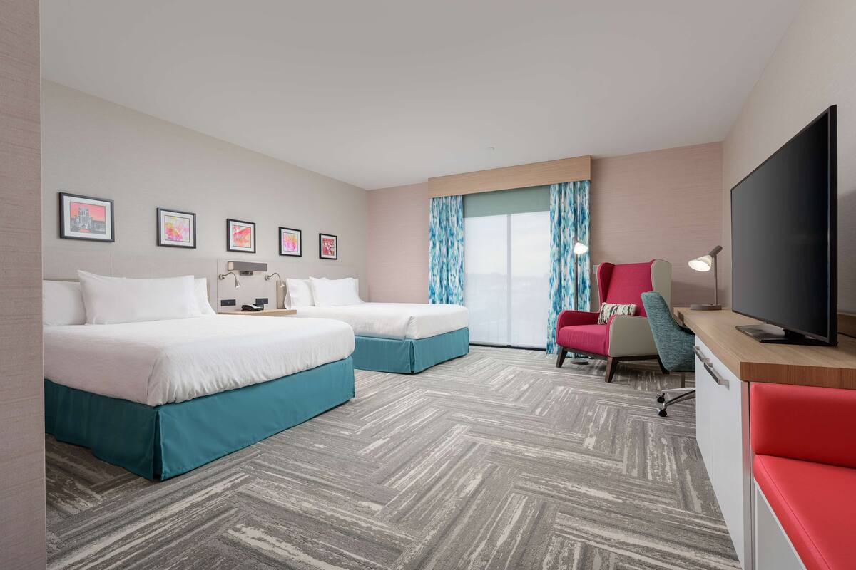 Habitación de hotel con dos camas, televisión, escritorio y ventana con cortinas.