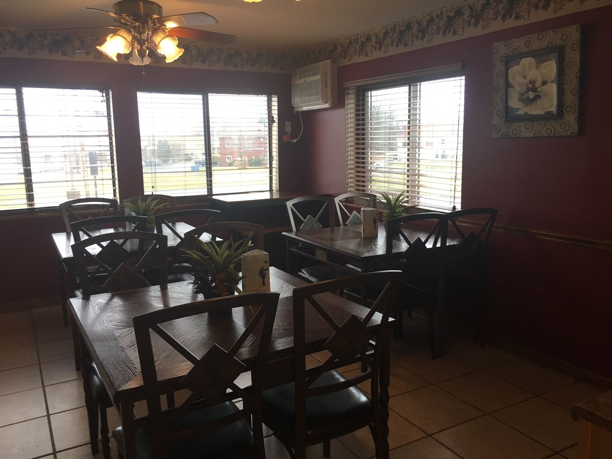 A dining area with a large table and chairs, large windows with blinds, a ceiling fan, and a wall-mounted air conditioner.