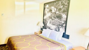A hotel room with a bed, a nightstand, a lamp, and a large framed picture on the wall.