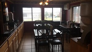 A restaurant with a dining area featuring a large table and chairs, a ceiling fan, and large windows with blinds.