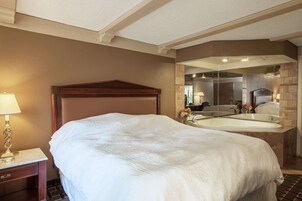 A hotel room with a large bed, a nightstand with a lamp, and a bathroom with a bathtub and sink.