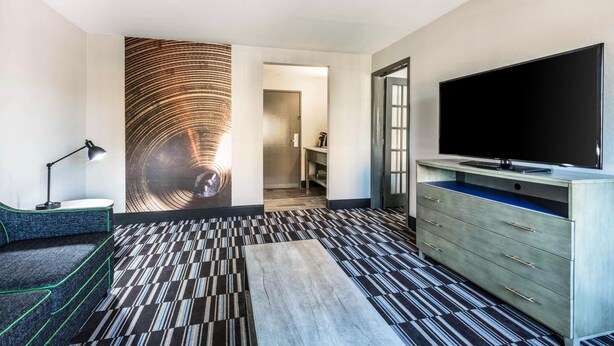 A hotel room with a large flat-screen TV, a sofa, a desk with a lamp, and a patterned carpet. - Comfort Inn Memphis Airport West (Memphis)