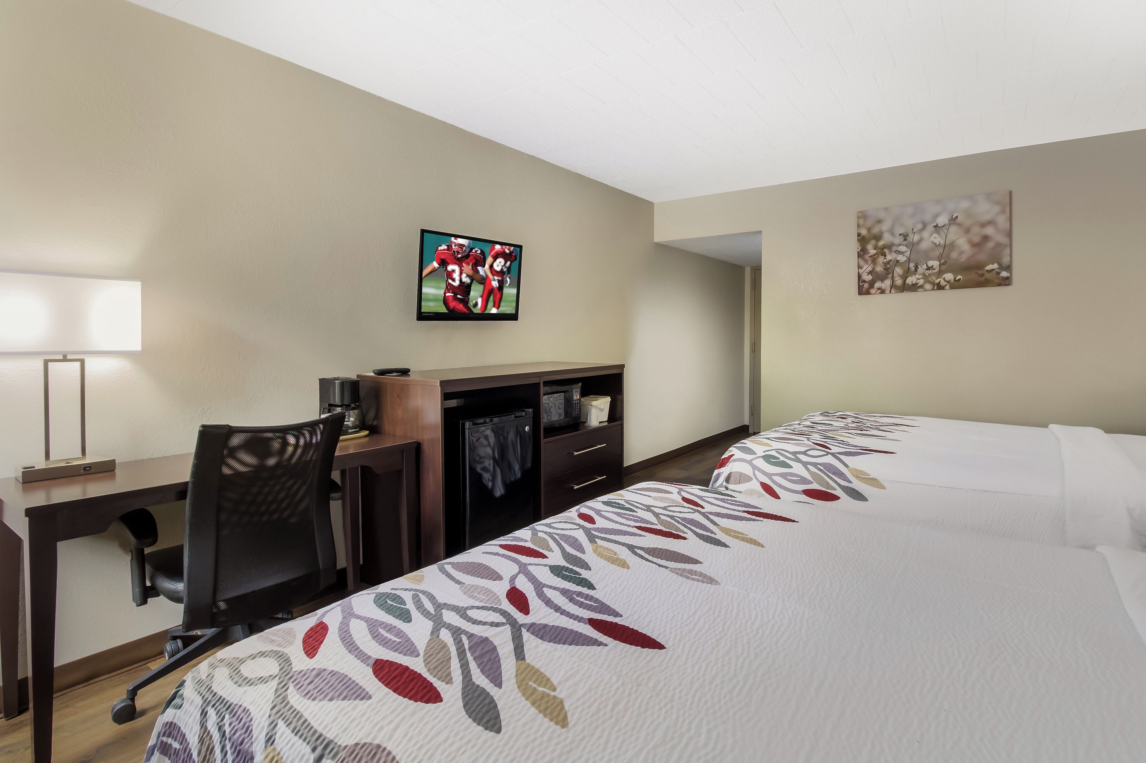 Una habitación de hotel con escritorio, silla, televisión y dos camas.
